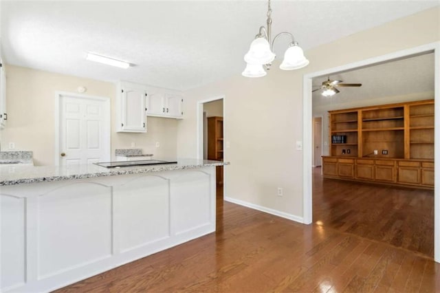 kitchen with light stone counters, dark wood-style flooring, hanging light fixtures, white cabinets, and a peninsula