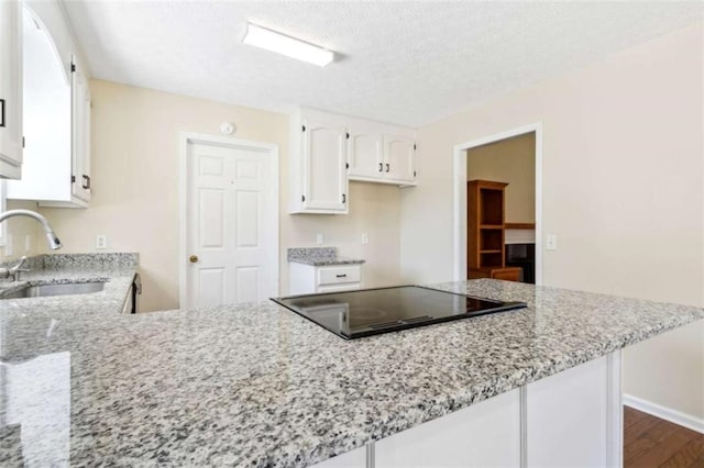 kitchen featuring black electric stovetop, a sink, white cabinets, and light stone countertops