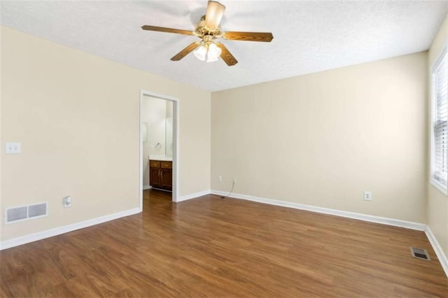 empty room featuring a ceiling fan, wood finished floors, visible vents, and baseboards