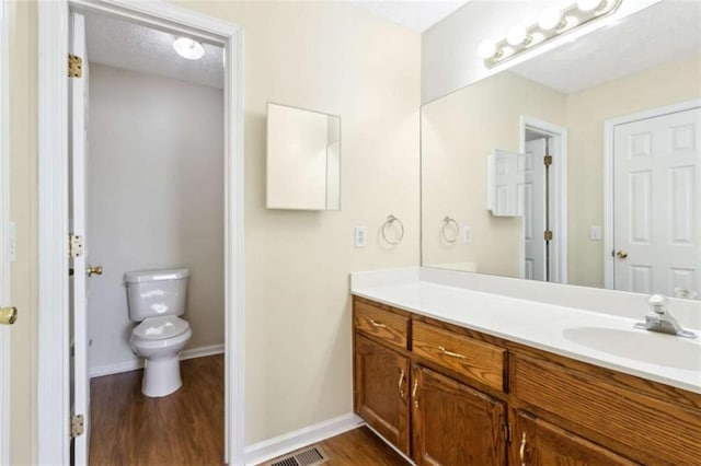 bathroom with visible vents, toilet, vanity, wood finished floors, and baseboards