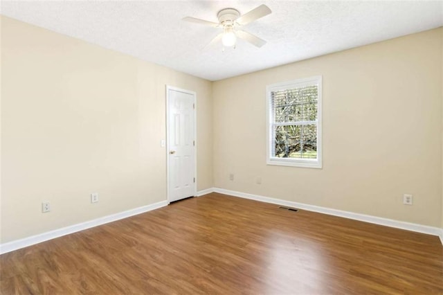 empty room with a ceiling fan, wood finished floors, visible vents, and baseboards