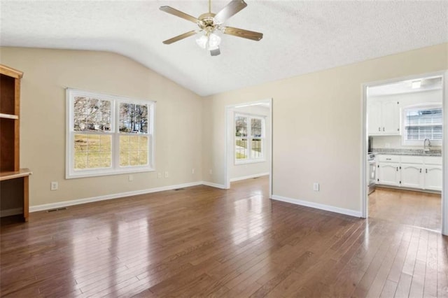 unfurnished living room with vaulted ceiling, ceiling fan, dark wood finished floors, and baseboards