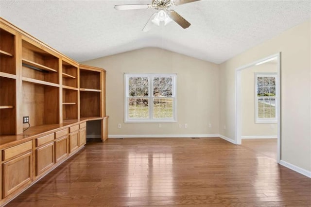 spare room featuring vaulted ceiling, built in desk, a textured ceiling, and wood-type flooring