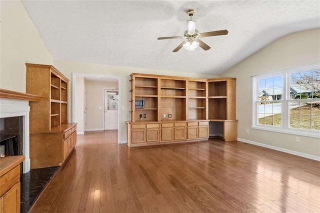 unfurnished living room with dark wood-style floors, a high end fireplace, built in study area, vaulted ceiling, and baseboards