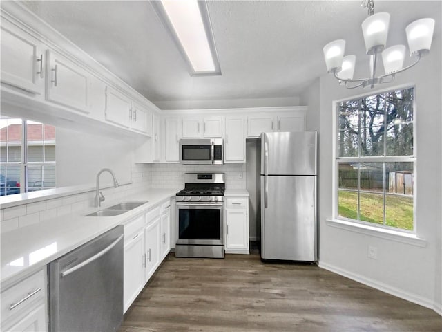 kitchen with backsplash, white cabinets, hanging light fixtures, appliances with stainless steel finishes, and a notable chandelier