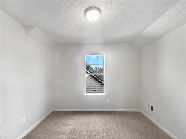 empty room featuring a textured ceiling, carpet, and vaulted ceiling