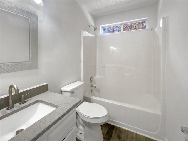 full bathroom with washtub / shower combination, hardwood / wood-style floors, a textured ceiling, toilet, and vanity