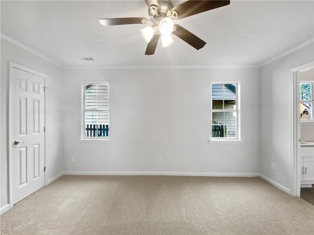 empty room with a wealth of natural light, ceiling fan, light colored carpet, and ornamental molding