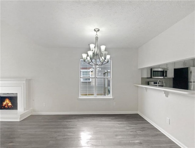 unfurnished dining area featuring a textured ceiling, dark hardwood / wood-style flooring, and an inviting chandelier