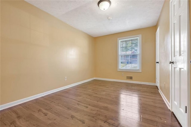 spare room with visible vents, a textured ceiling, baseboards, and wood finished floors