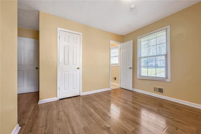 unfurnished bedroom with visible vents, baseboards, a textured ceiling, and wood finished floors