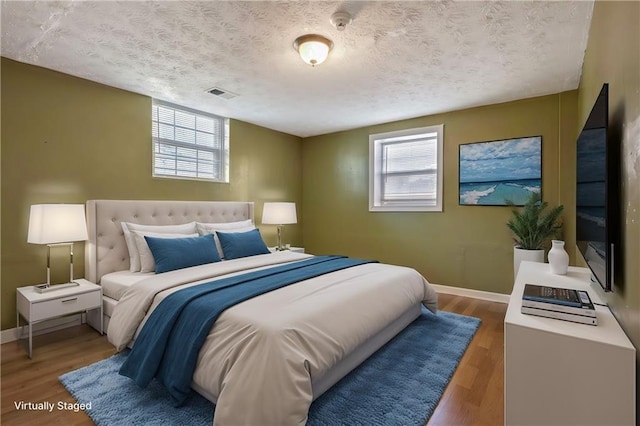 bedroom featuring a textured ceiling, wood finished floors, visible vents, and baseboards