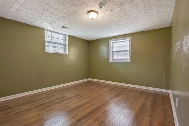 empty room with visible vents, a textured ceiling, baseboards, and hardwood / wood-style floors