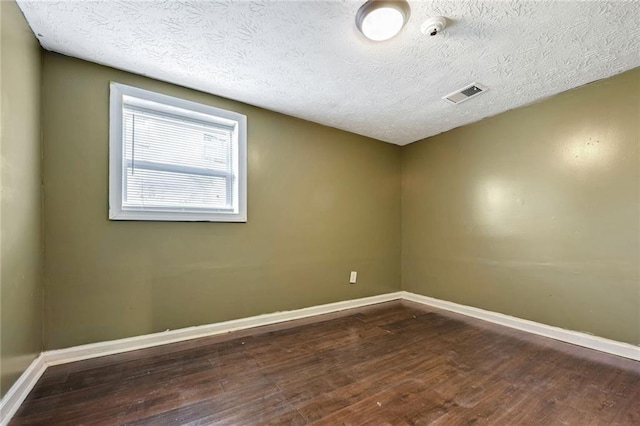 spare room with visible vents, baseboards, dark wood-type flooring, and a textured ceiling