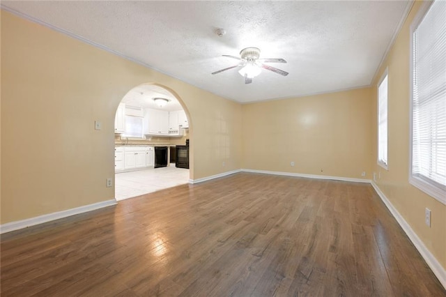 unfurnished living room featuring ceiling fan, baseboards, wood finished floors, arched walkways, and a textured ceiling