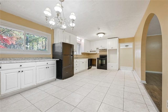 kitchen with light tile patterned floors, arched walkways, black appliances, white cabinets, and under cabinet range hood