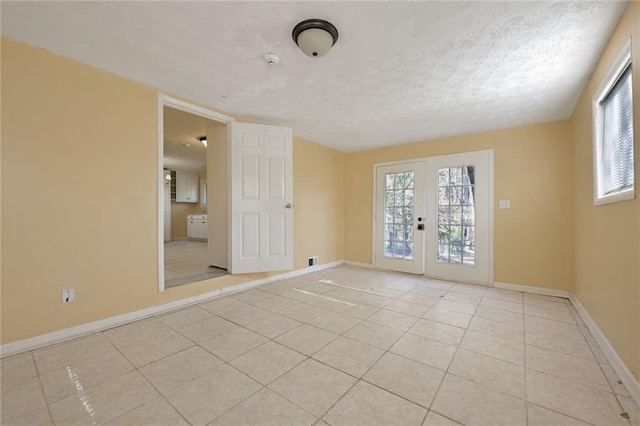 empty room with light tile patterned floors, french doors, a textured ceiling, and baseboards