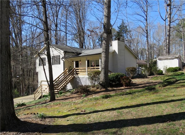 view of front of home featuring a front lawn, stairs, a chimney, a storage shed, and an outdoor structure