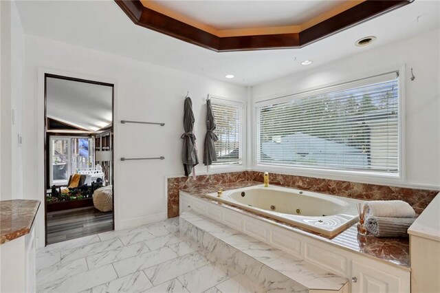 bathroom featuring a healthy amount of sunlight, a bath, and a tray ceiling