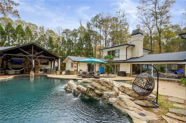 view of swimming pool with pool water feature, an outdoor kitchen, a patio, and an outdoor living space with a fire pit