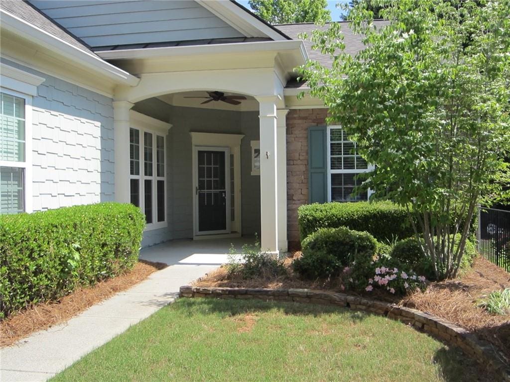 doorway to property with ceiling fan, a shingled roof, and stone siding