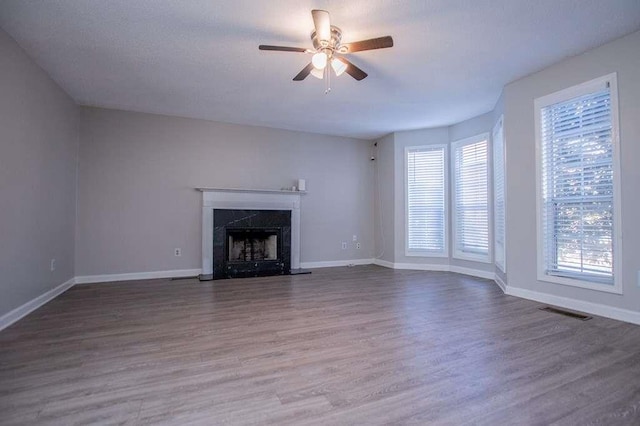 unfurnished living room featuring wood-type flooring, a premium fireplace, and ceiling fan