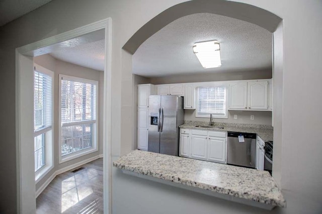 kitchen with sink, white cabinetry, a textured ceiling, appliances with stainless steel finishes, and light stone countertops