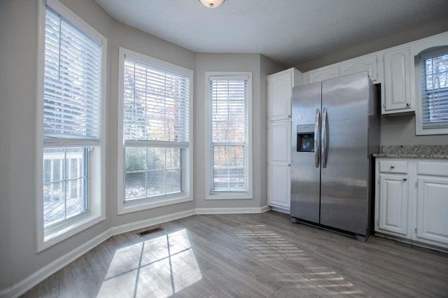 kitchen with light stone countertops, white cabinets, light wood-type flooring, and stainless steel fridge with ice dispenser