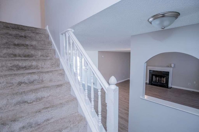 staircase with a high end fireplace and a textured ceiling