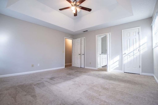 unfurnished bedroom with ensuite bath, light colored carpet, a raised ceiling, and ceiling fan