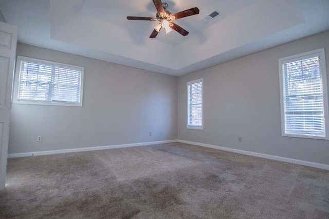 empty room featuring a tray ceiling, ceiling fan, and carpet flooring