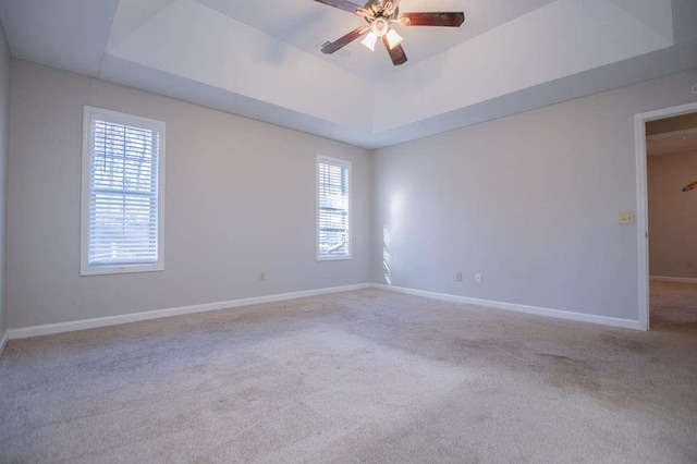 unfurnished room with ceiling fan, plenty of natural light, a raised ceiling, and light carpet