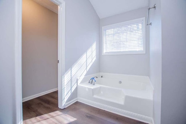 bathroom featuring vaulted ceiling, wood-type flooring, a tub, and a textured ceiling