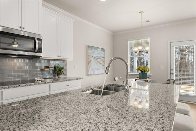 kitchen with stainless steel microwave, a sink, tasteful backsplash, white cabinetry, and ornamental molding