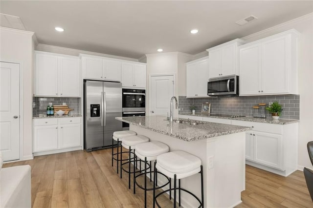 kitchen featuring a breakfast bar, stainless steel appliances, light wood-style floors, a sink, and white cabinetry