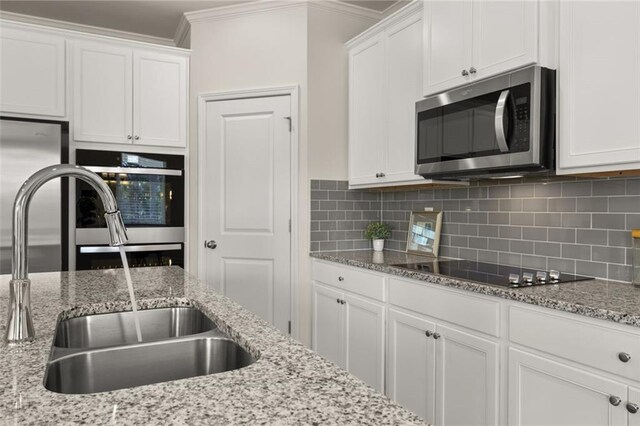 kitchen featuring white cabinetry, tasteful backsplash, crown molding, a sink, and appliances with stainless steel finishes