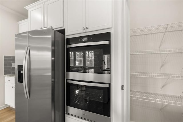 kitchen with decorative backsplash, stainless steel appliances, white cabinets, light wood-type flooring, and crown molding
