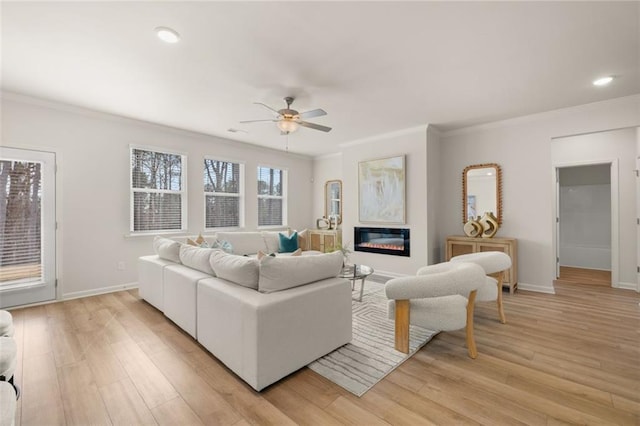 living room featuring crown molding, ceiling fan, light wood-style floors, and a glass covered fireplace
