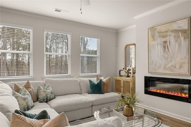 living area with visible vents, baseboards, a glass covered fireplace, ornamental molding, and wood finished floors