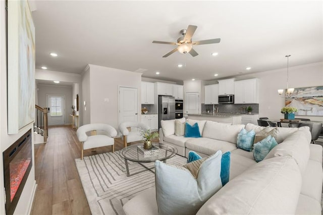 living area featuring light wood-style floors, ornamental molding, stairs, and ceiling fan with notable chandelier