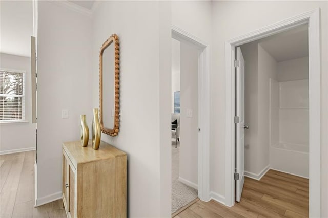 corridor with ornamental molding, light wood finished floors, and baseboards