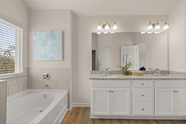 full bath with double vanity, a garden tub, baseboards, and a sink