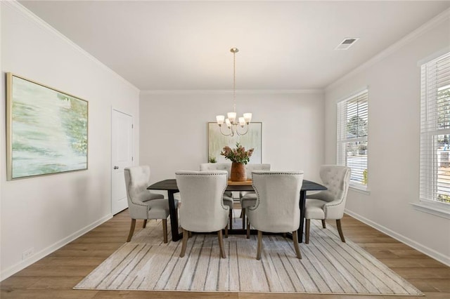 dining room with ornamental molding, an inviting chandelier, visible vents, and wood finished floors