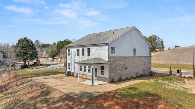 rear view of property featuring a yard, a patio area, central air condition unit, and brick siding
