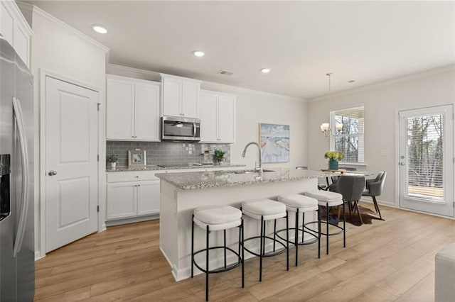 kitchen with white cabinets, a sink, stainless steel appliances, light wood-type flooring, and backsplash