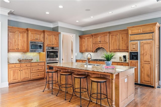 kitchen featuring built in appliances, a kitchen island with sink, light stone countertops, and ornamental molding