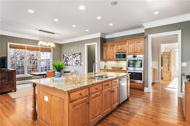 kitchen with light stone counters, stainless steel appliances, sink, pendant lighting, and a center island with sink