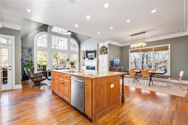 kitchen featuring light stone countertops, stainless steel dishwasher, a kitchen island with sink, sink, and hanging light fixtures