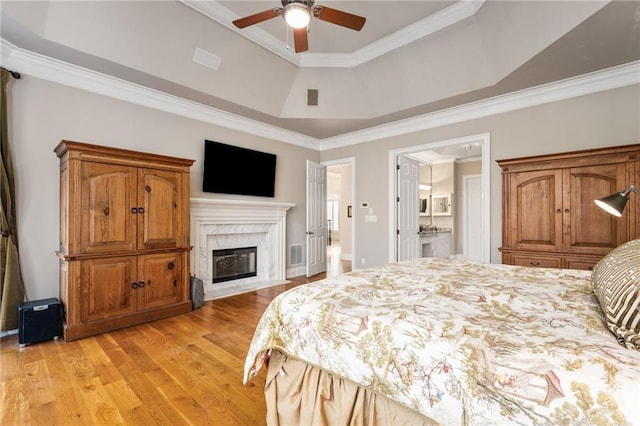 bedroom featuring ceiling fan, a raised ceiling, a high end fireplace, ensuite bathroom, and ornamental molding