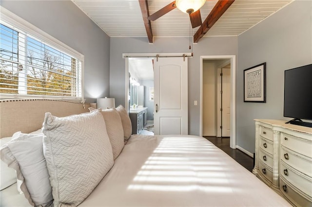 bedroom featuring baseboards, beam ceiling, dark wood-style flooring, a barn door, and connected bathroom